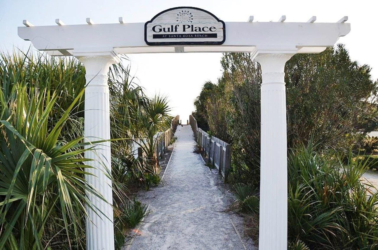 A pathway leading to a white pergola with a sign reading 'Gulf Place at Santa Rosa Beach.'
