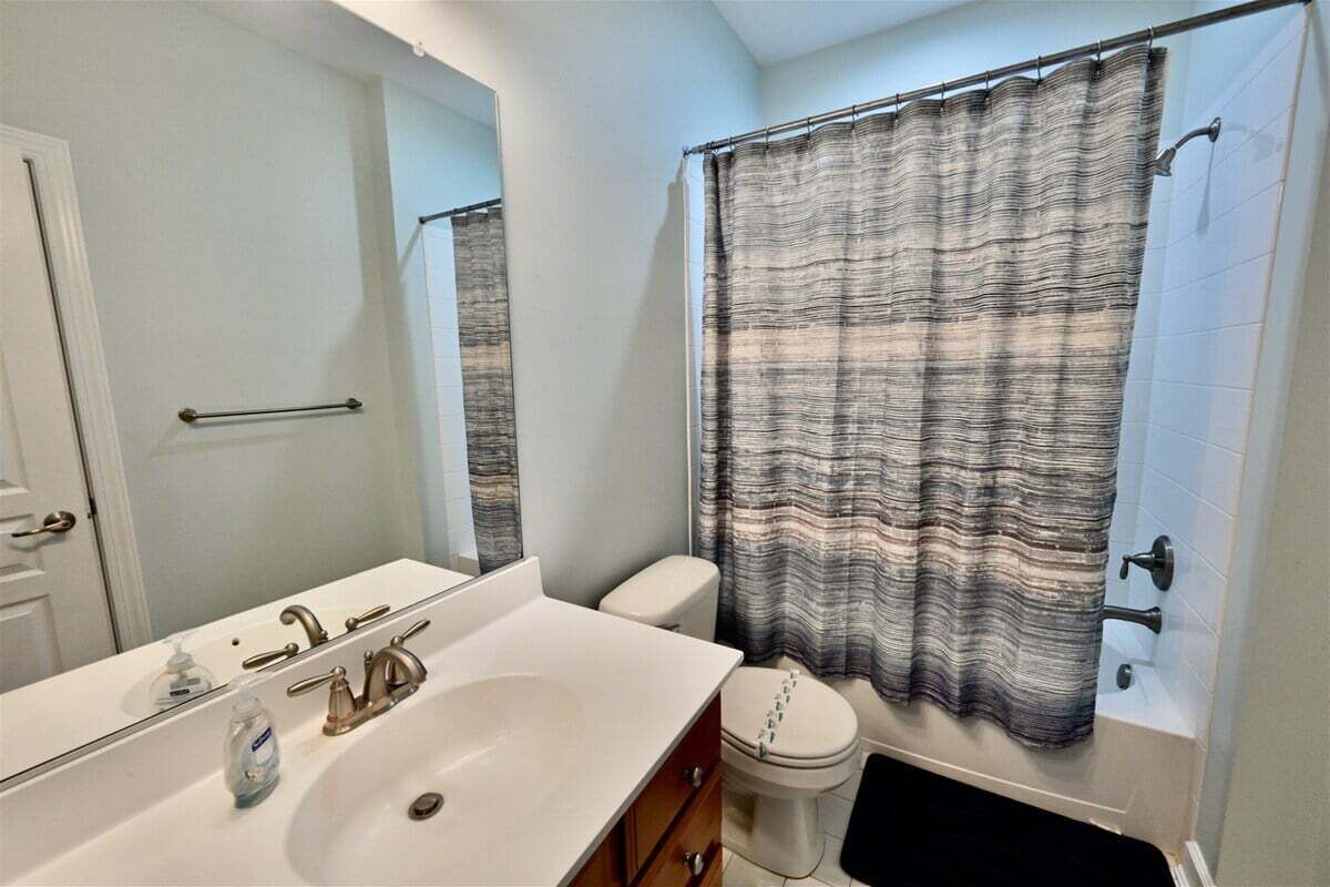 A bathroom with a white sink, a mirror, a toilet, and a shower curtain.