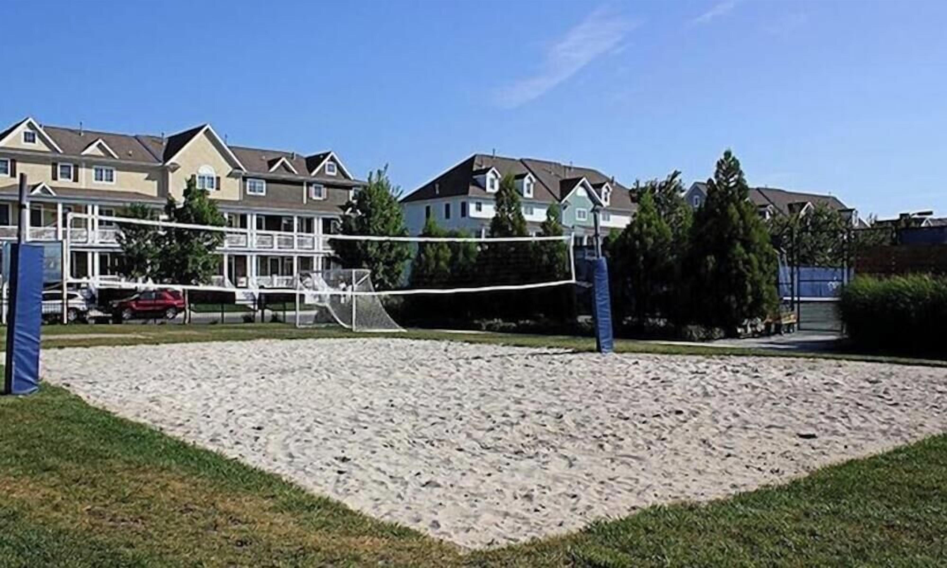 A sandy volleyball court with net, surrounded by houses.