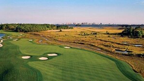 Campo de golf con búnkeres, obstáculos de agua y un horizonte urbano de fondo.