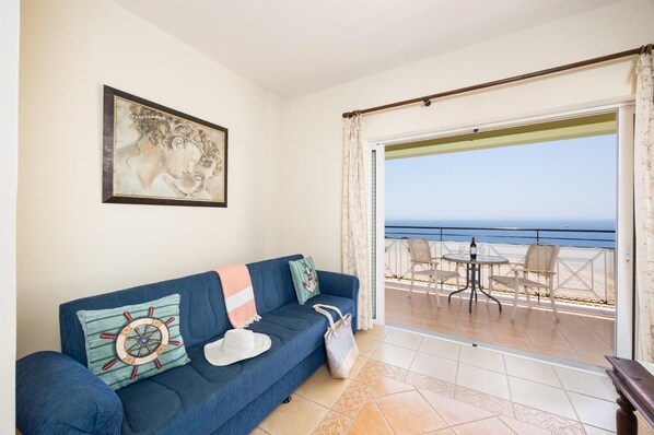 Habitació amb un sofà blau, un quadre i vista al mar a través d'un balcó.