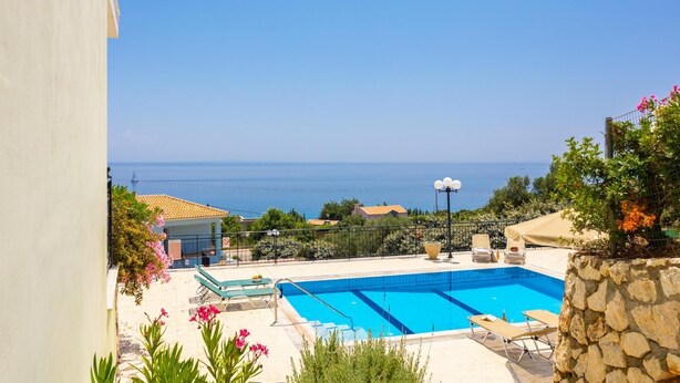 A swimming pool with a view of the sea, surrounded by greenery and a stone wall. - Skala Villa Green - Three Bedroom Villa, Sleeps 6 (Ionian Islands)