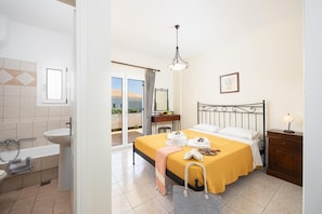 Habitación de hotel con cama, mesita de noche, baño con lavabo e inodoro, y puerta corrediza de vidrio que da a un balcón.