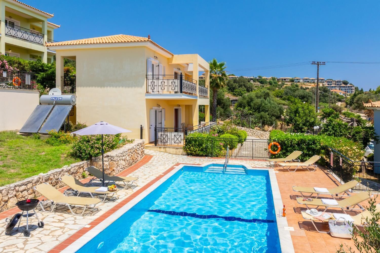 A swimming pool with lounge chairs, a barbecue grill, and a stone wall.