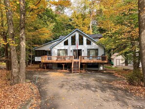 A two-story cabin with a deck, surrounded by trees with autumn foliage.