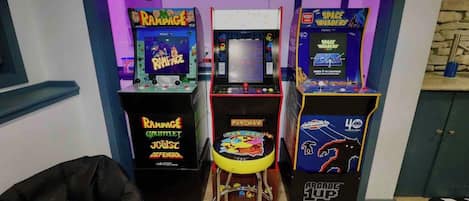 Arcade machines, a stool, and a neon sign in a room.
