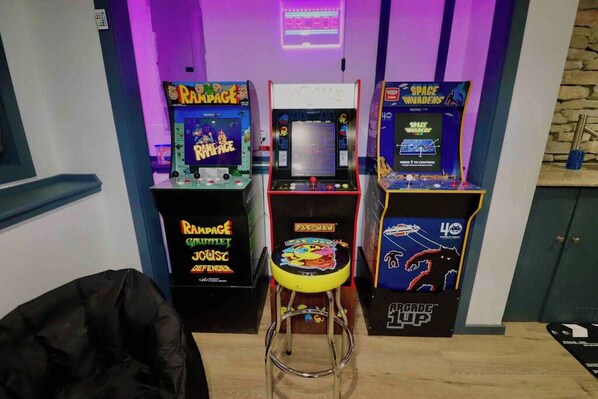 Une borne d’arcade, un tabouret et un panneau lumineux au néon dans une pièce.