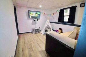 Une pièce comprenant un lit, un téléviseur fixé au mur, une tente de jeu et une petite table.