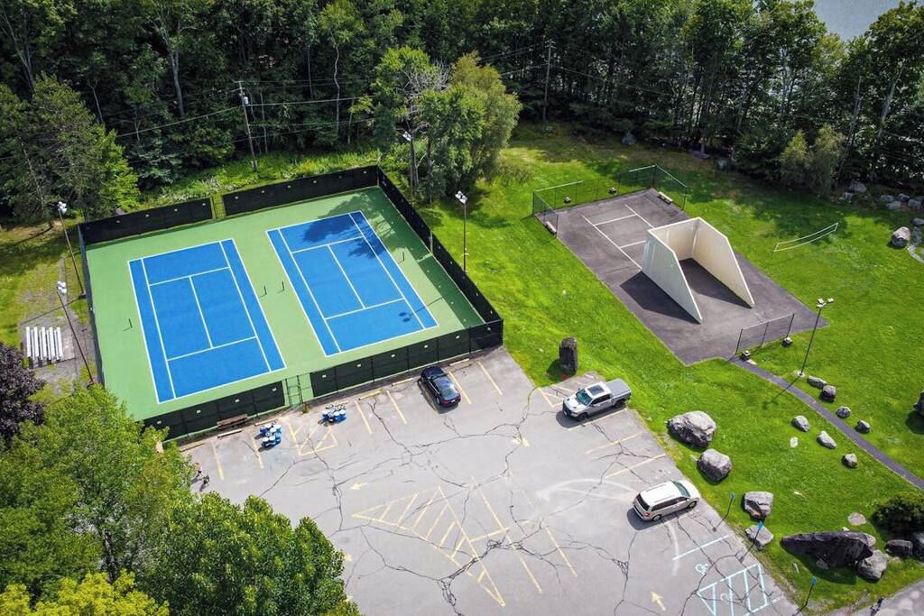 Een tennisbaan buiten, met een parkeerplaats en een klein paviljoen.