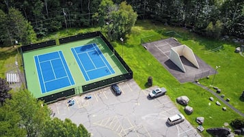 Een tennisbaan buiten, met een parkeerplaats en een klein paviljoen.