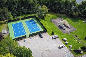 Een tennisbaan buiten, met een parkeerplaats en een klein paviljoen.