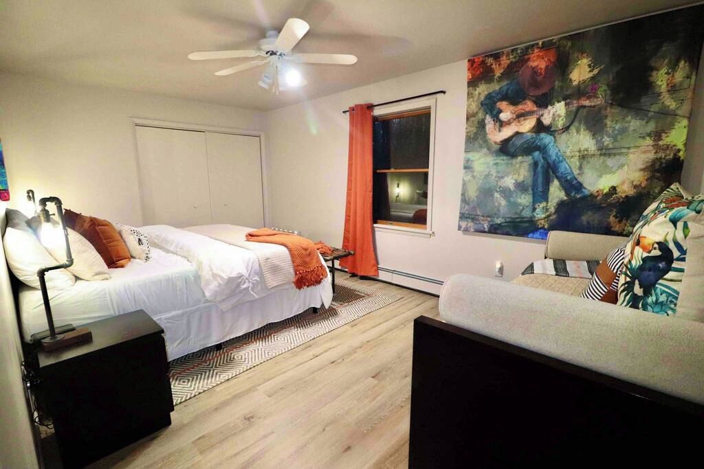 A bedroom with two beds, a ceiling fan, a large painting, and a window with curtains.