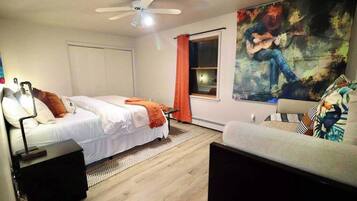A bedroom with two beds, a ceiling fan, a large painting, and a window with curtains.