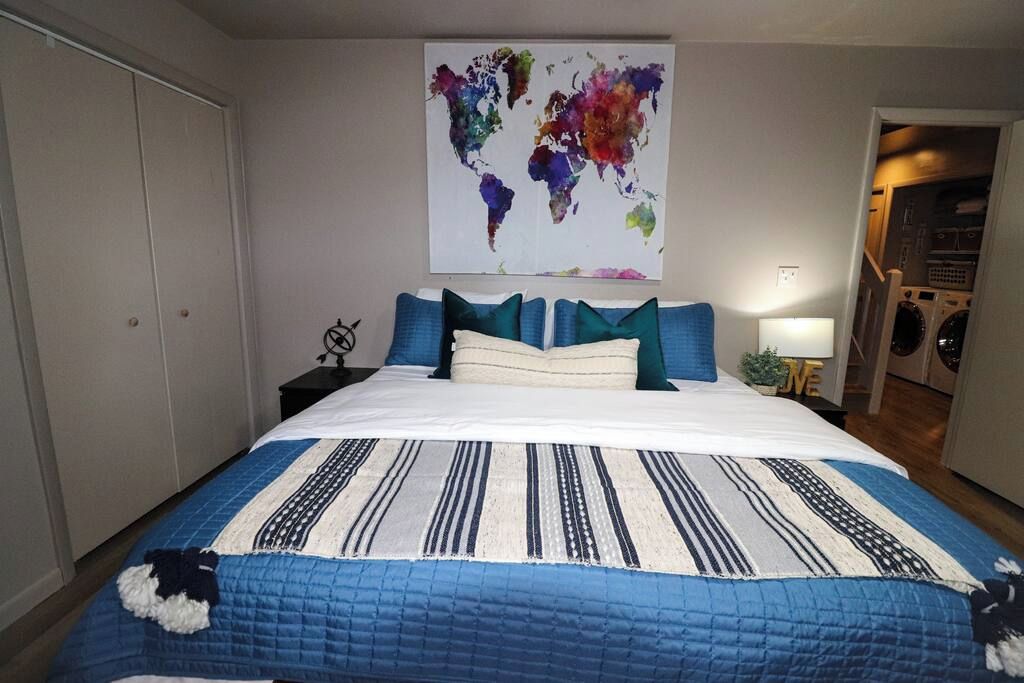A bedroom with a bed, pillows, a world map artwork, a nightstand, and a lamp.