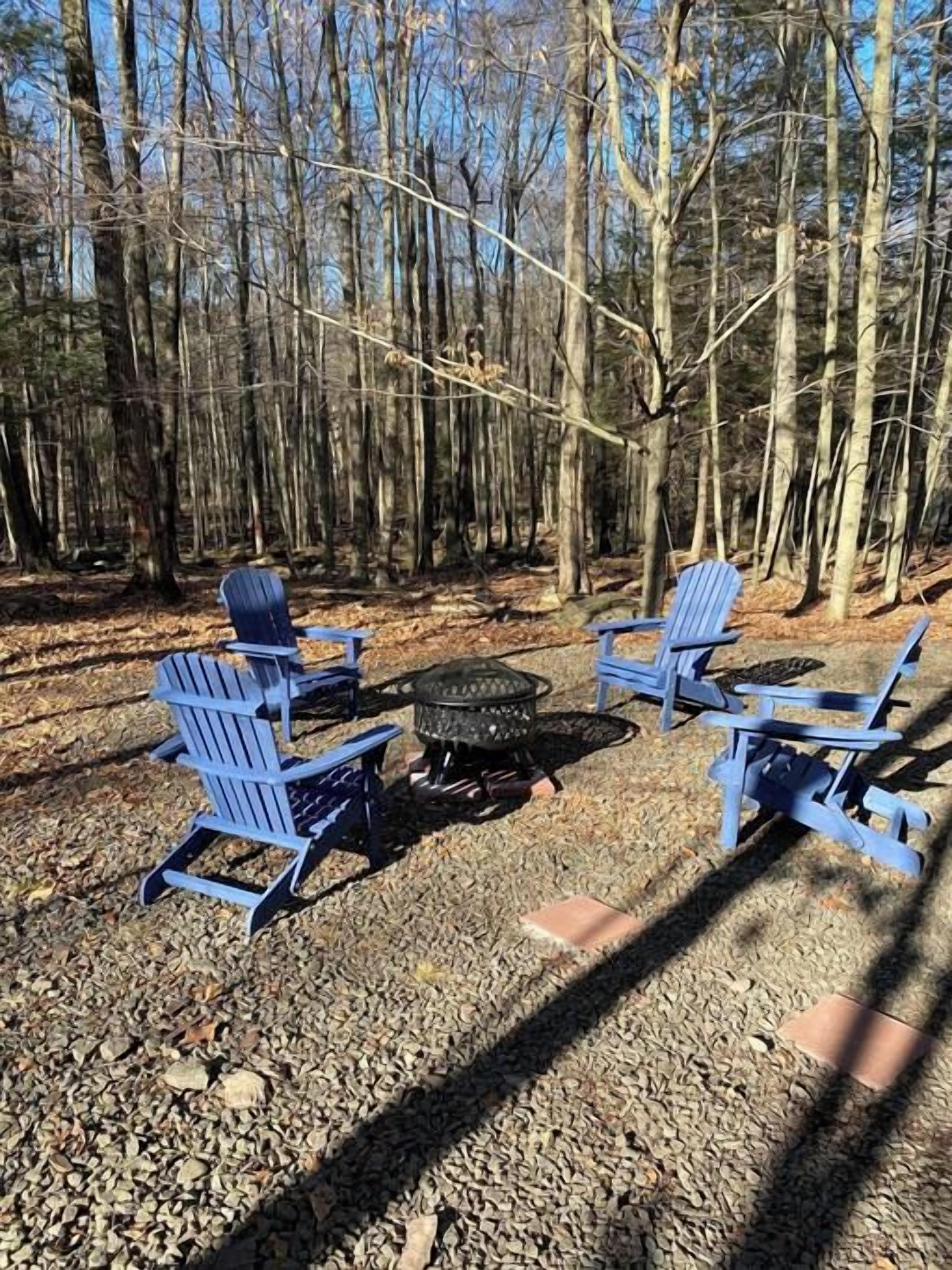 Un terrain de camping avec quatre chaises Adirondack bleues disposées autour d’un foyer central.