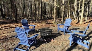 Un terrain de camping avec quatre chaises Adirondack bleues disposées autour d’un foyer central.