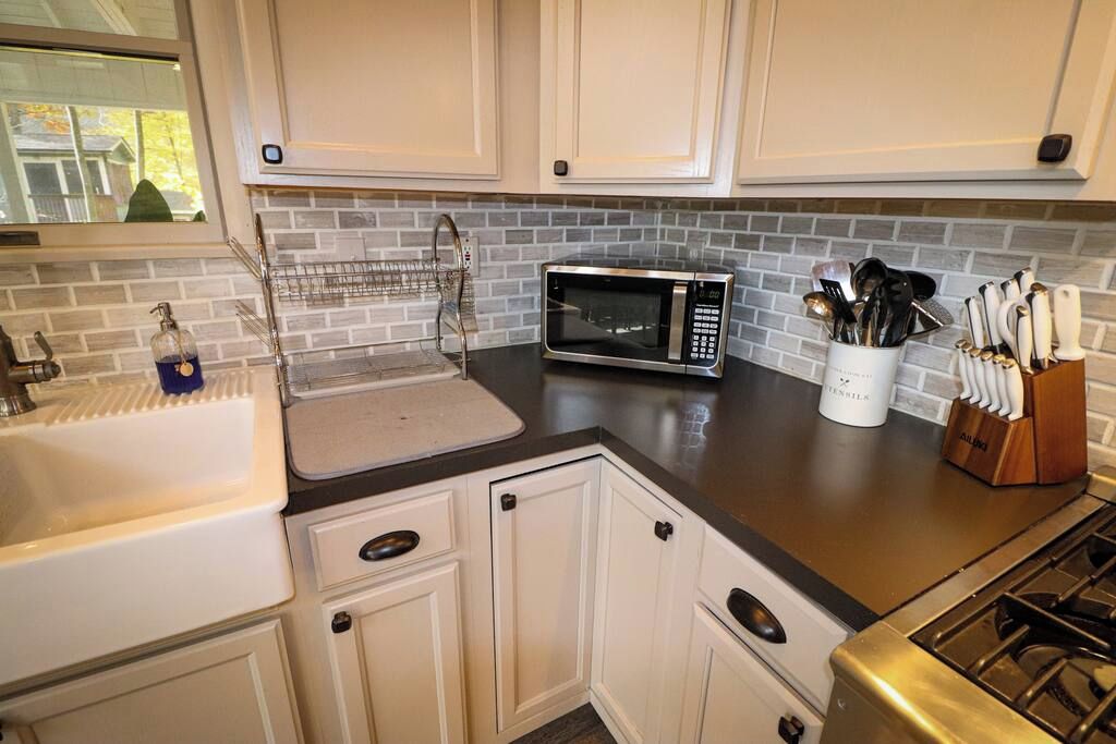 A kitchen with white cabinets, a microwave, a sink, and a utensil holder.