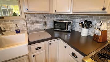 A kitchen with white cabinets, a microwave, a sink, and a utensil holder.