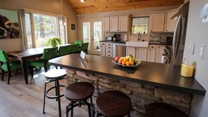 Una cocina moderna con una isla central, una zona de comedor con sillas verdes y una pared de acento de piedra.