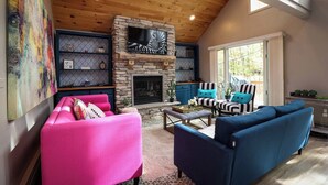 Un salon chaleureux avec une cheminée en pierre, un grand téléviseur et des fauteuils aux couleurs vives.
