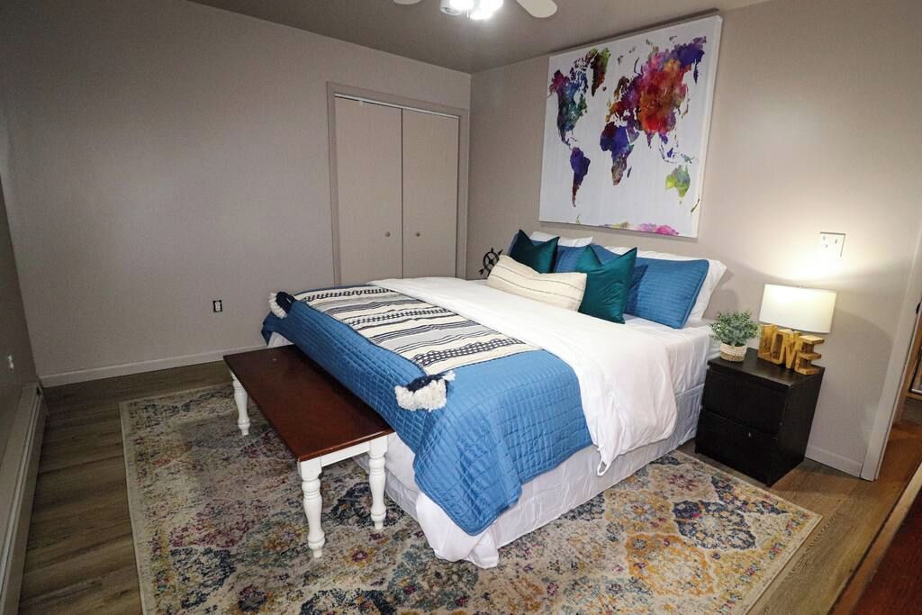 Un dormitorio con cama, una banca, un mesita de noche, una lámpara y un mapa del mundo en la pared.