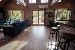 A cozy interior with a sofa, dining area, and large windows offering a view of the outdoors. - Villa MiaNova: A Modern Hideout in the Woods. (Lake Ariel)