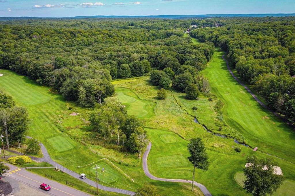 An aerial view of a golf course with multiple fairways, a clubhouse, and surrounding wooded areas.