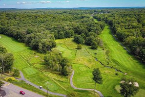 Eine Vogelperspektive eines Golfplatzes mit mehreren Fairways, einem Clubhaus und umliegenden bewaldeten Gebieten.