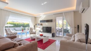 Ein modernes Wohnzimmer mit Fernseher, Sofa und Blick auf einen Pool.