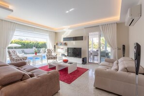 Ein modernes Wohnzimmer mit Fernseher, Sofa und Blick auf einen Pool.