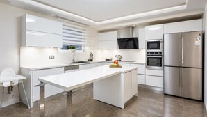 Une cuisine moderne avec des meubles blancs, un îlot central, un réfrigérateur en acier inoxydable et un four à micro-ondes.