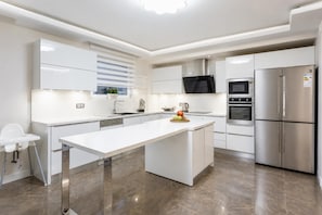 Een moderne keuken met witte kasten, een centraal eiland, een roestvrijstalen koelkast en een magnetron.