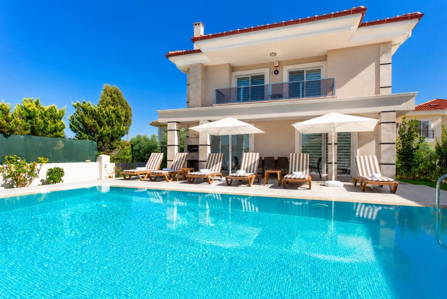 Una casa moderna de dos pisos con piscina, sillas de sol y sombrillas.
