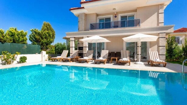 Une maison moderne à deux étages, dotée d’une piscine, de chaises longues et de parasols.