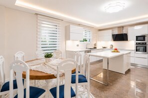 Eine moderne Küche mit weißen Schränken, einer zentralen Kochinsel und einem Essbereich mit Holztisch und weißen Stühlen.