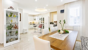 Uma sala de jantar moderna com uma mesa de madeira, cadeiras brancas e um aparador de vidro com objetos decorativos.