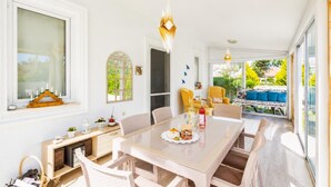 Um quarto claro com uma mesa de jantar, cadeiras, um sofá e uma janela com vista para o verde.