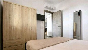 A bedroom with a large wooden wardrobe, a bed with a beige bedspread, and a mirror on the wall. - Casterly Rock by Alpha Living (Mykonos)