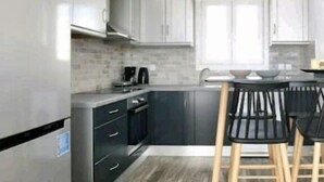 A modern kitchen with grey cabinets, a black countertop, and a wooden dining area with two chairs. - Casterly Rock by Alpha Living (Mykonos)