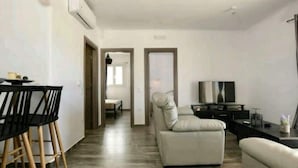 A modern living room with a sofa, a TV, and a dining area with chairs and a table. - Casterly Rock by Alpha Living (Mykonos)