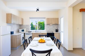 Une cuisine moderne avec une table à manger pour quatre personnes, un lave-linge et une fenêtre donnant sur un espace verdoyant.