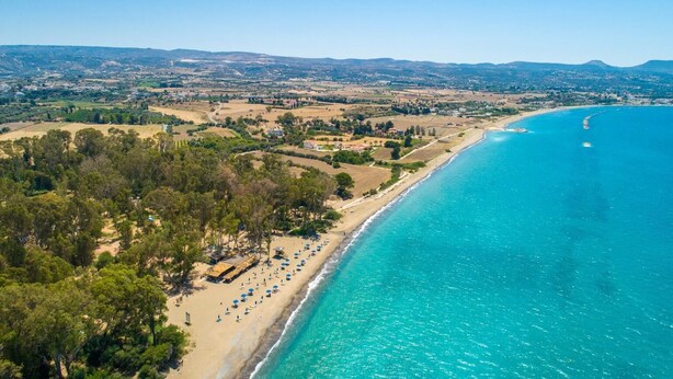 An aerial view of a coastal area with a beach, clear blue waters, and a mix of residential and agricultural land in the background. - Sun Beach Villa Thio (Poli Crysochous)
