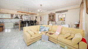 A living room with a beige sofa, a glass coffee table, and a dining area with a table and chairs.