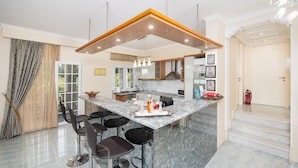A modern kitchen with a marble island, bar stools, and pendant lighting.