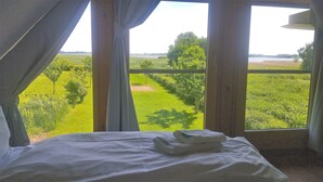 A bed with a neatly folded towel, a view of a green field through large windows, and a clear sky. - Einfach Urlaub auf Rügen (Groß Schoritz)