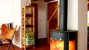A cozy room with a wood-burning stove, a chair, a shelf with blankets, and a metal bucket. - Einfach Urlaub auf Rügen (Groß Schoritz)