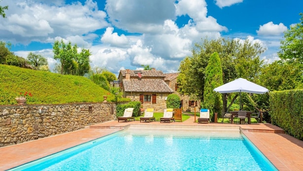A swimming pool with lounge chairs and umbrellas, surrounded by a stone wall and greenery. - Villa Bramasole Large Private Pool, WiFi (Sinalunga)