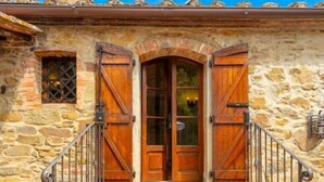 A stone building with a wooden door and two large wooden shutters, a set of brick steps leading up to the entrance, and a metal railing on the left side. - Villa Bramasole Large Private Pool, WiFi (Sinalunga)