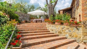 A stone staircase leading to a covered outdoor area with a table and chairs, surrounded by potted plants and trees. - Villa Bramasole Large Private Pool, WiFi (Sinalunga)