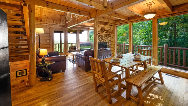 A wooden cabin interior with a dining area, a fireplace, and large windows overlooking greenery. - Free Attractions | Secluded, New Hot Tub w/ Views, Fireplace, Pet-Friendly (Gatlinburg)